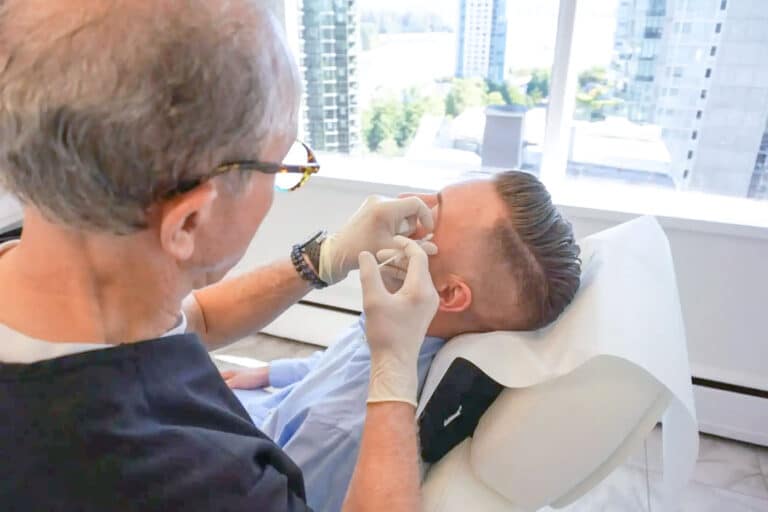 Dr. Morrell stands over a patient performing a cosmetic procedure while explaining the difference between dermal fillers and botox