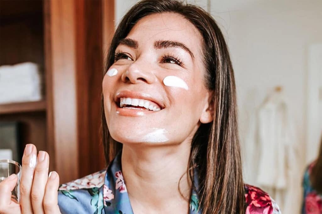 A woman smiling with moisturizer on her face, demonstrating simple tips to improve skin health